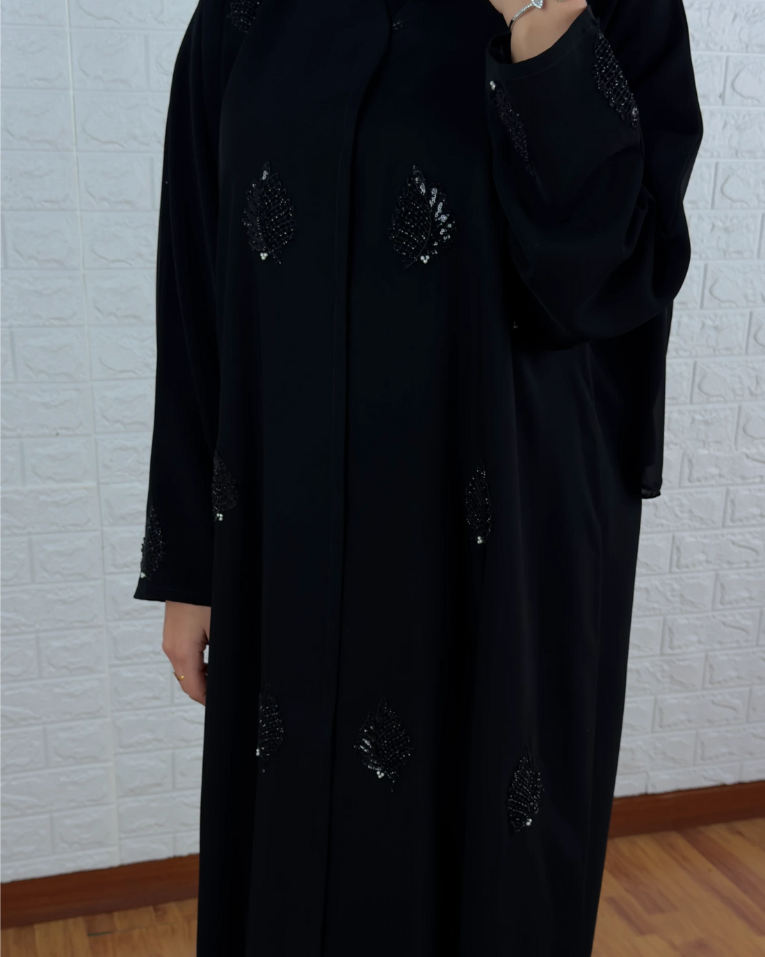 Person wearing a long black coat with decorative buttons against a light brick wall.